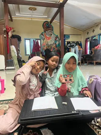 Tiga anak perempuan duduk di depan meja kecil saat kegiatan belajar bersama