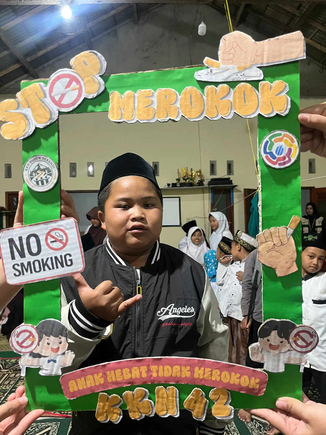Seorang anak berpeci berpose di dalam bingkai hijau kampanye stop merokok